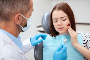 girl with tooth pain sitting in dental chair with dentist helping